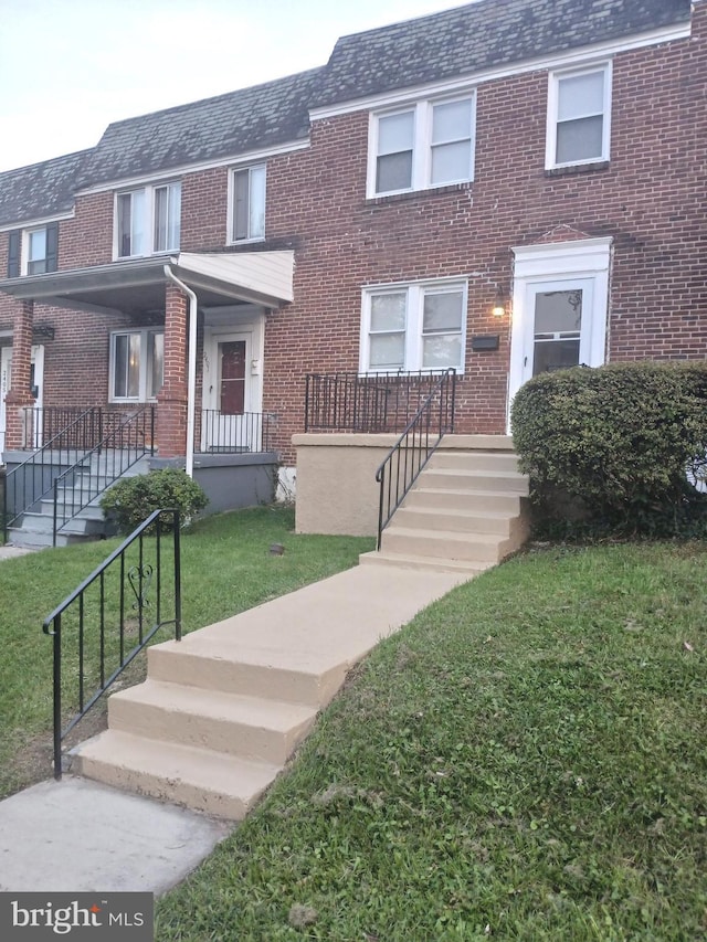 townhome / multi-family property featuring covered porch, a front yard, mansard roof, and brick siding