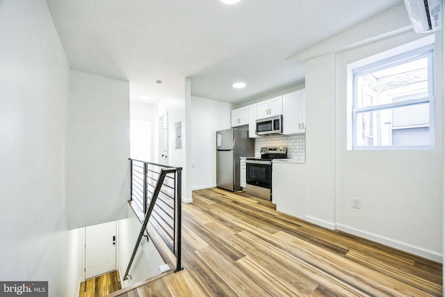 kitchen featuring tasteful backsplash, stainless steel appliances, light wood-type flooring, and white cabinets