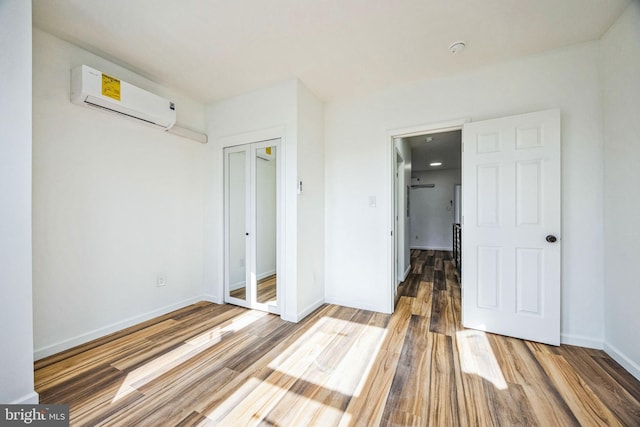 unfurnished bedroom featuring a wall mounted air conditioner, hardwood / wood-style floors, and a closet