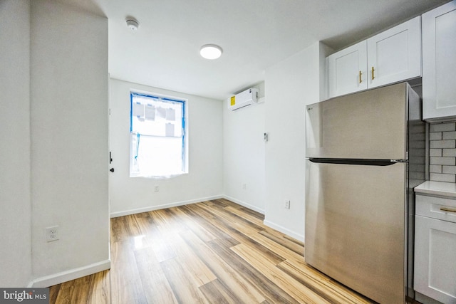 kitchen featuring an AC wall unit, light wood-type flooring, stainless steel fridge, decorative backsplash, and white cabinets