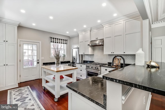 kitchen with white cabinetry, stainless steel appliances, dark hardwood / wood-style floors, kitchen peninsula, and dark stone counters