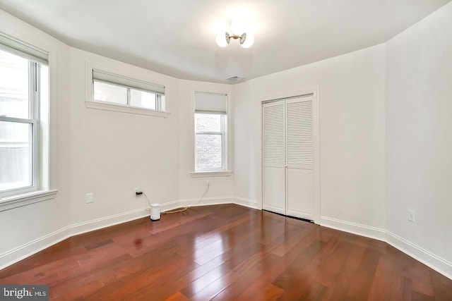 unfurnished bedroom with multiple windows, dark wood-type flooring, and a closet