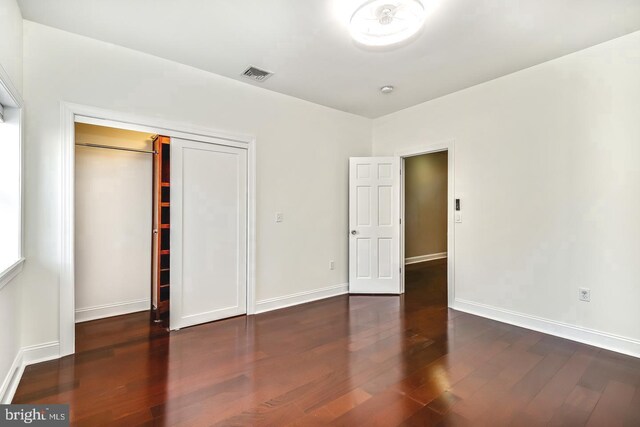 unfurnished bedroom with baseboards, a closet, visible vents, and dark wood-type flooring