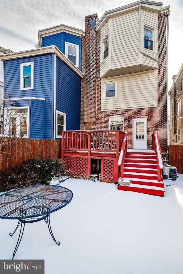 snow covered rear of property with brick siding, a chimney, fence, a deck, and cooling unit