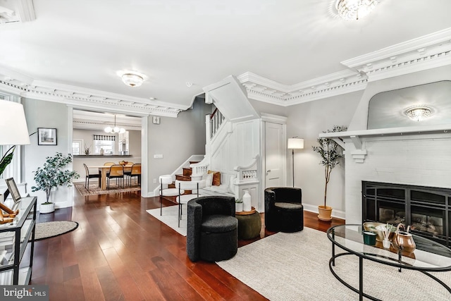 living area featuring dark wood-style floors, a fireplace, stairway, and ornamental molding