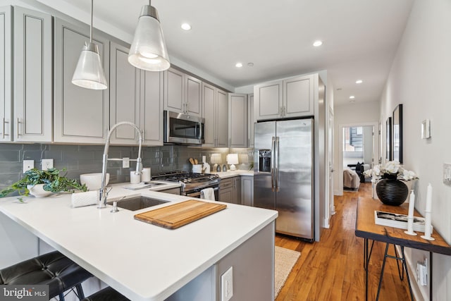 kitchen with pendant lighting, stainless steel appliances, kitchen peninsula, and gray cabinetry