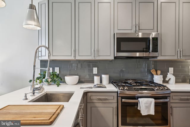 kitchen with sink, gray cabinetry, decorative light fixtures, appliances with stainless steel finishes, and decorative backsplash