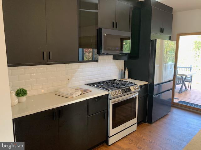 kitchen featuring black refrigerator, backsplash, stainless steel range with gas cooktop, and light wood-type flooring