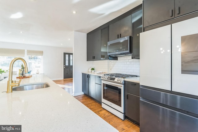 kitchen featuring sink, backsplash, light stone counters, stainless steel appliances, and light wood-type flooring