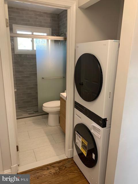 bathroom featuring stacked washing maching and dryer, tile patterned flooring, vanity, an enclosed shower, and toilet