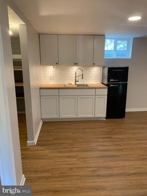 kitchen featuring white cabinetry, black fridge, sink, and light hardwood / wood-style floors