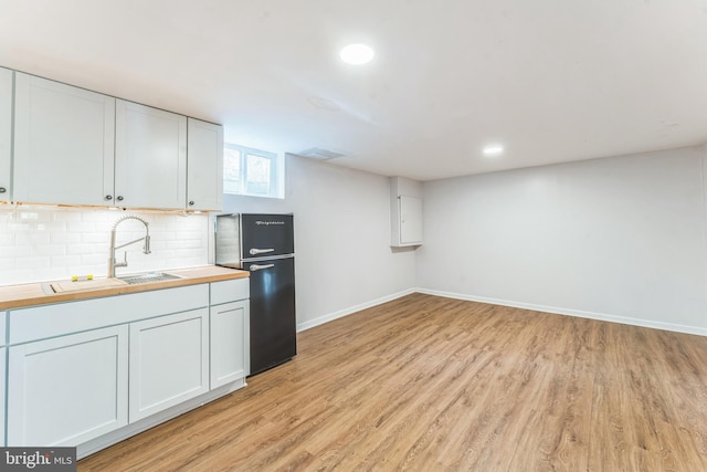 kitchen with white cabinetry, butcher block countertops, black refrigerator, and sink