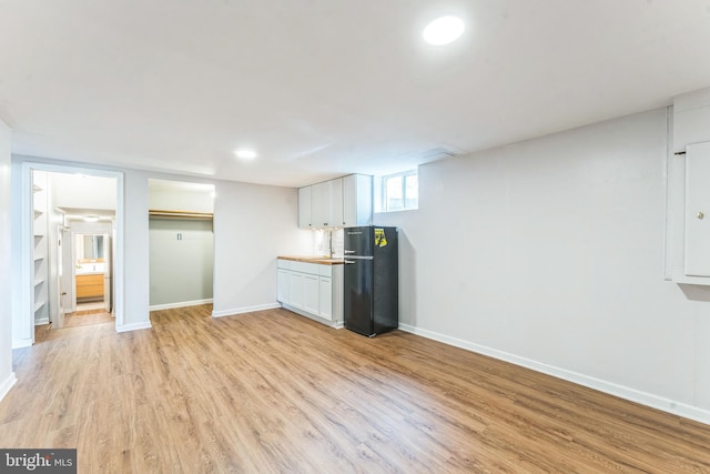 kitchen with white cabinetry, black fridge, and light wood-type flooring