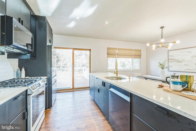 kitchen with sink, decorative light fixtures, light hardwood / wood-style flooring, appliances with stainless steel finishes, and backsplash