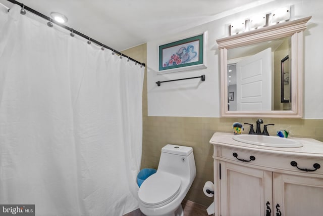 bathroom with toilet, a wainscoted wall, tile walls, and vanity