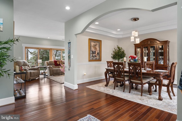 dining space with a tray ceiling, dark wood finished floors, a notable chandelier, recessed lighting, and baseboards