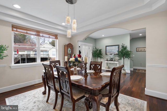 dining space featuring dark wood-style floors, arched walkways, a tray ceiling, recessed lighting, and baseboards