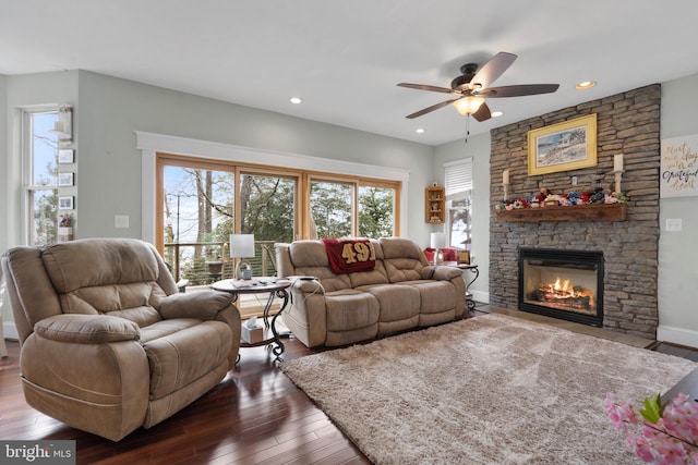 living room featuring dark wood-style floors, recessed lighting, a stone fireplace, and baseboards