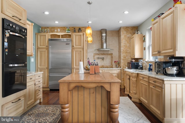 kitchen with dobule oven black, wall chimney exhaust hood, hanging light fixtures, stainless steel built in refrigerator, and light brown cabinets