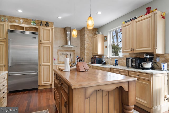 kitchen with decorative backsplash, wall chimney exhaust hood, a kitchen island, pendant lighting, and built in fridge