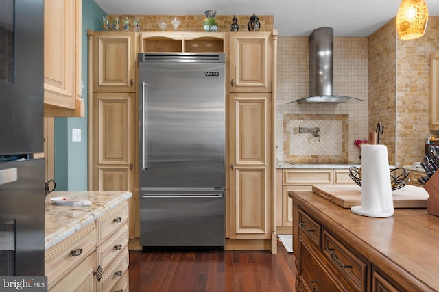 kitchen featuring built in fridge, wall chimney range hood, decorative backsplash, dark wood finished floors, and pendant lighting