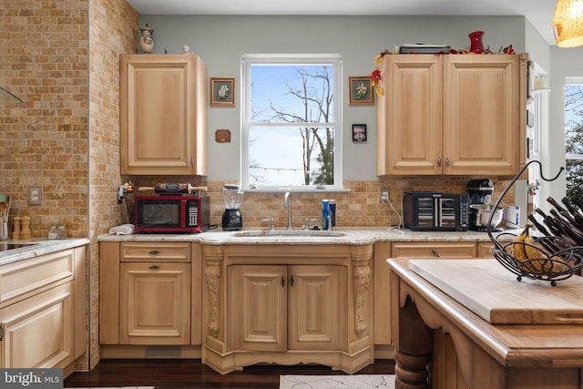 kitchen featuring tasteful backsplash, light brown cabinetry, a sink, brick wall, and light stone countertops