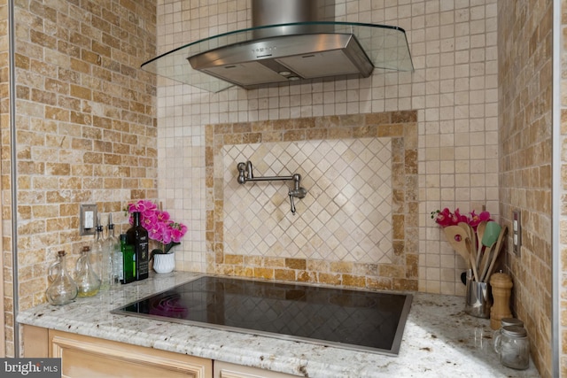 interior space featuring black electric stovetop, light stone counters, light brown cabinets, exhaust hood, and tasteful backsplash