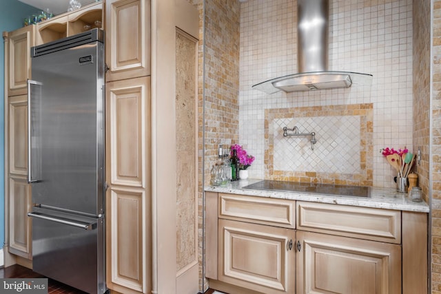 kitchen featuring stainless steel built in fridge, black electric stovetop, light stone counters, and wall chimney range hood