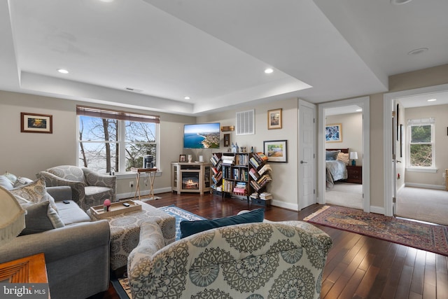 living area with a warm lit fireplace, a raised ceiling, visible vents, and wood-type flooring