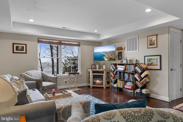 living room featuring a tray ceiling, dark wood-type flooring, and visible vents