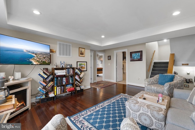 living area featuring dark wood-type flooring, a warm lit fireplace, visible vents, and stairway