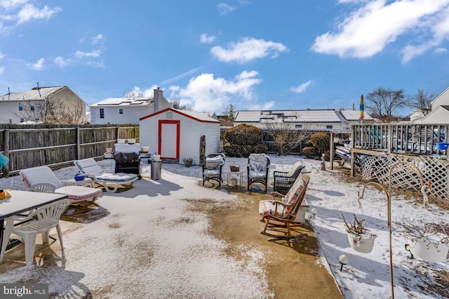 snow covered patio featuring a wooden deck and a storage unit