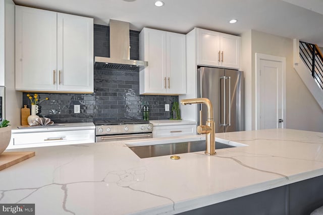 kitchen featuring wall chimney range hood, sink, appliances with stainless steel finishes, light stone countertops, and white cabinets