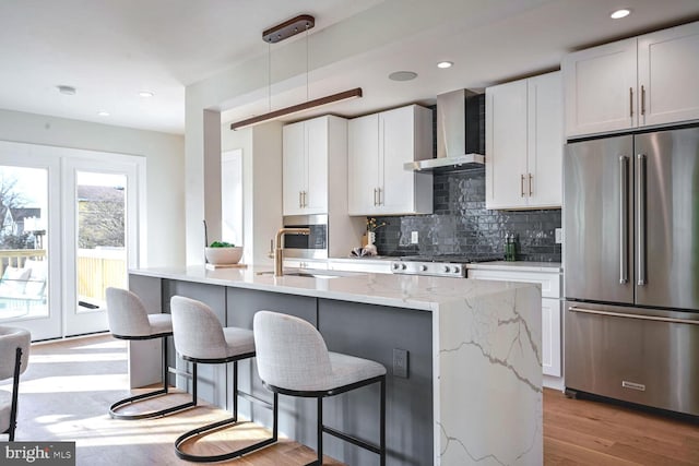 kitchen with pendant lighting, white cabinets, high end refrigerator, and wall chimney range hood