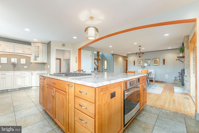 kitchen with pendant lighting, light tile patterned floors, appliances with stainless steel finishes, light stone counters, and a large island with sink