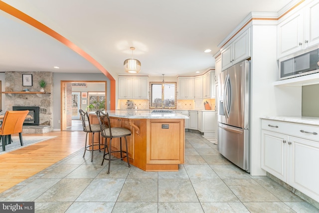 kitchen featuring a kitchen island, appliances with stainless steel finishes, pendant lighting, a breakfast bar area, and light stone countertops