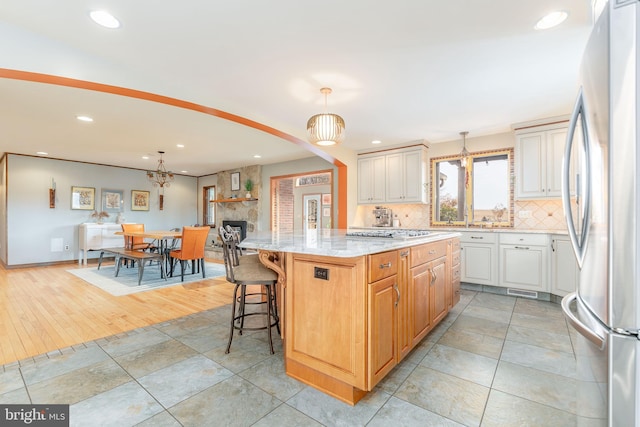 kitchen featuring hanging light fixtures, a kitchen island, stainless steel appliances, light stone countertops, and backsplash