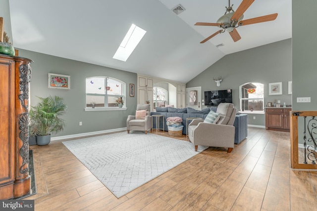 living room featuring ceiling fan, vaulted ceiling with skylight, light hardwood / wood-style flooring, and a wealth of natural light