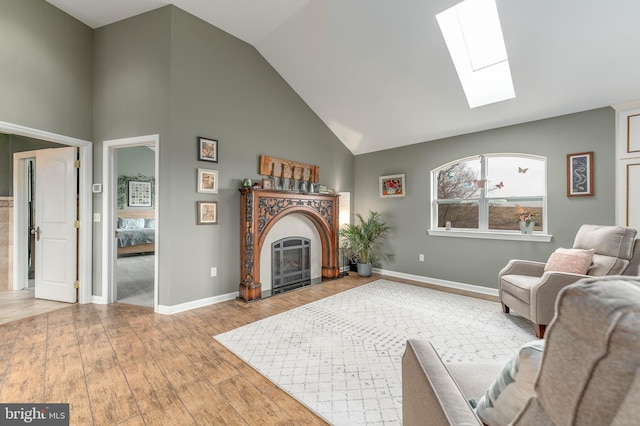 living room with high vaulted ceiling, a skylight, and light hardwood / wood-style floors