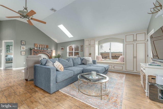 living room featuring ceiling fan, a skylight, high vaulted ceiling, and light wood-type flooring