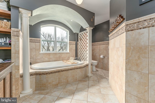 bathroom with toilet, decorative columns, tile walls, tiled bath, and tile patterned flooring