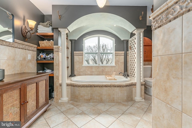 bathroom featuring tiled tub, tile walls, tile patterned floors, toilet, and ornate columns