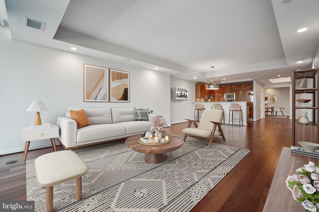 living room featuring dark wood-type flooring and a tray ceiling