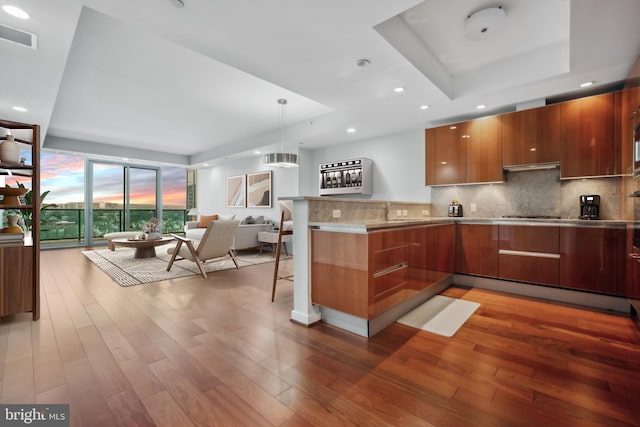 kitchen with hanging light fixtures, kitchen peninsula, a kitchen bar, decorative backsplash, and a raised ceiling