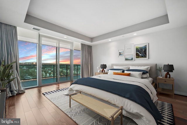 bedroom featuring hardwood / wood-style flooring, floor to ceiling windows, access to exterior, and a raised ceiling