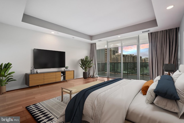 bedroom with wood-type flooring, a tray ceiling, floor to ceiling windows, and access to outside