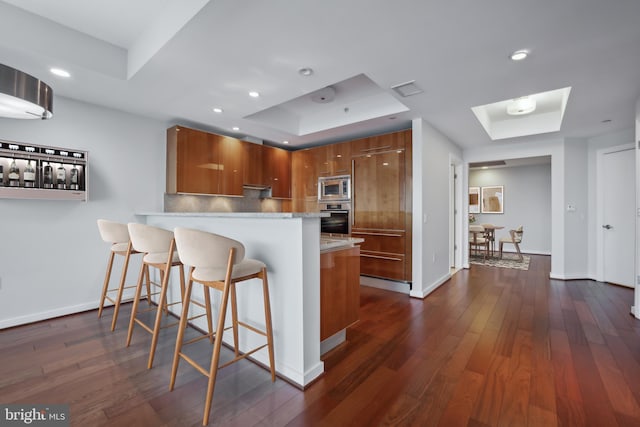 kitchen featuring dark wood-type flooring, appliances with stainless steel finishes, backsplash, a tray ceiling, and kitchen peninsula