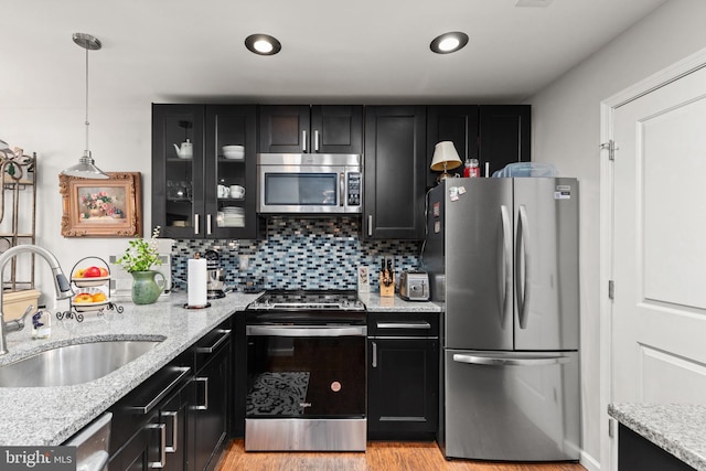 kitchen featuring sink, tasteful backsplash, decorative light fixtures, stainless steel appliances, and light stone countertops