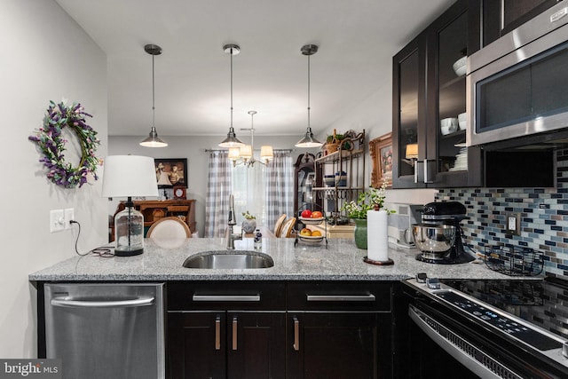 kitchen with pendant lighting, sink, appliances with stainless steel finishes, tasteful backsplash, and light stone countertops