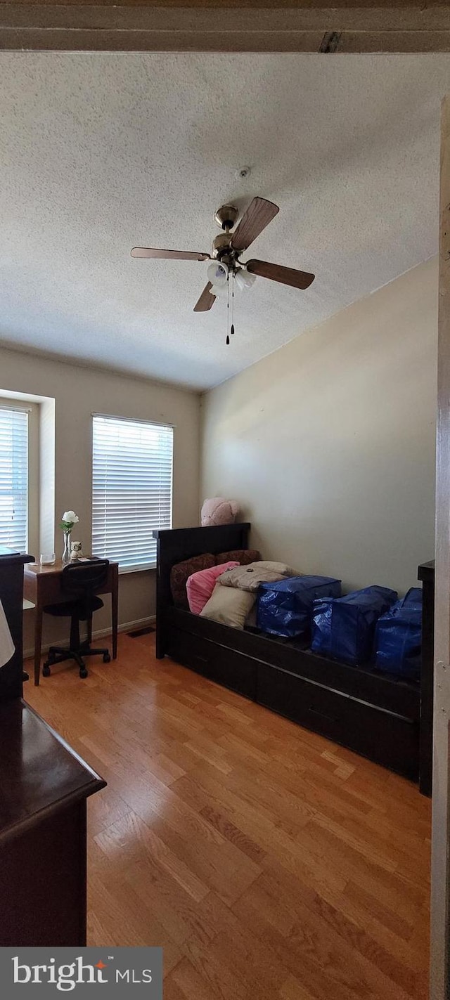 bedroom featuring a textured ceiling, multiple windows, a ceiling fan, and wood finished floors